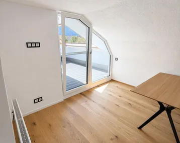 Heller Raum im Dachgeschoss mit Holzboden, Heizkörper und Zugang zu einem Balkon.