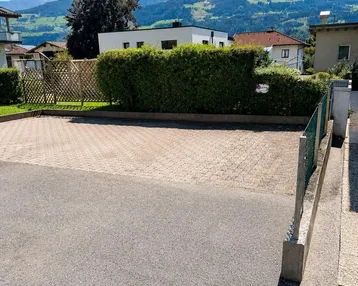 Außenparkplatz mit gepflasterter Fläche, Hecke und malerischem Bergblick.