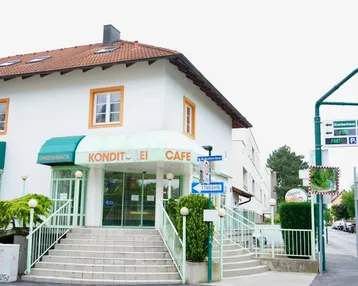 Weißes Gebäude mit rotem Ziegeldach, das eine Konditorei und ein Café beherbergt, mit einer Treppe zum Eingang.