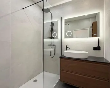 Modernes Badezimmer mit ebenerdiger Dusche, beleuchtetem Spiegel und elegantem Waschtischunterschrank.