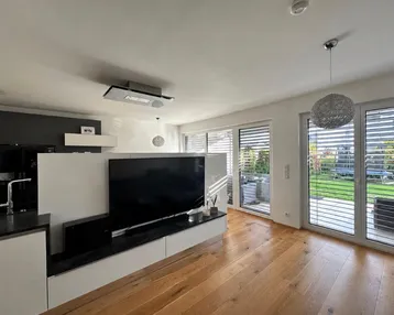 Helles Wohnzimmer mit Holzboden, großem Fernseher und direktem Zugang zum Gartenbereich.