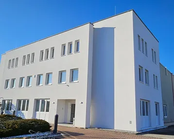Modernes dreistöckiges Bürogebäude mit weißer Fassade und vielen Fenstern unter blauem Himmel.