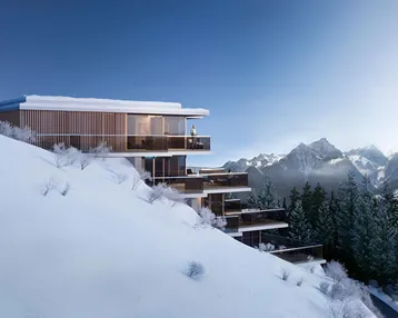 Moderne Architektur in den Bergen mit großen Glasfronten und Terrassen, umgeben von Schnee.