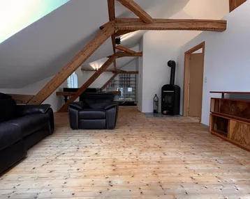 Gemütliches Wohnzimmer mit Holzbalken, Kaminofen und hellem Holzfußboden.