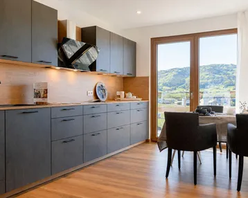 Moderne Küche mit dunklen Schränken, Holzakzenten und Essbereich mit Blick auf die grüne Landschaft.