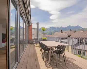 Geräumige Dachterrasse mit Holzboden, Esstisch und Stühlen, bietet einen weiten Blick auf die Berge.