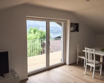 Heller Wohn- und Essbereich mit Holzboden, Dachschrägen und Zugang zu einem Balkon mit Seeblick.
