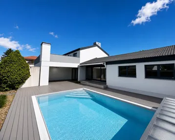 Modernes Haus mit privatem Swimmingpool und Holzterrasse unter blauem Himmel.