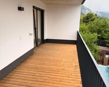 Geräumiger Balkon mit Holzboden und Blick auf die umliegende grüne Landschaft und Berge.