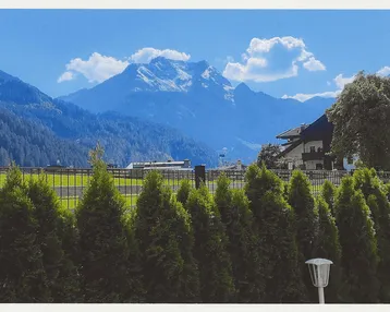 Panoramablick auf die majestätischen Berge unter blauem Himmel, umrahmt von einer grünen Hecke.