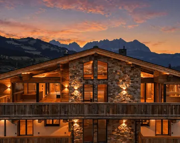 Beeindruckendes Chalet im alpinen Stil bei Sonnenuntergang mit beleuchteter Fassade und Bergblick.