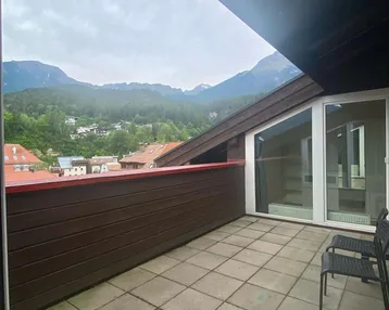 Große Terrasse mit Fliesenboden, Holzelementen und einem weiten Blick auf die Berge.