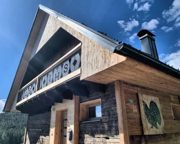 Traditionelles Holzchalet mit geschnitztem Balkongeländer und Blick auf die umliegende Natur.