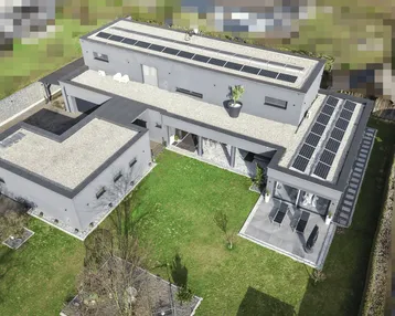 Luftaufnahme einer modernen Villa mit Flachdach, Solaranlagen und weitläufigem Garten.