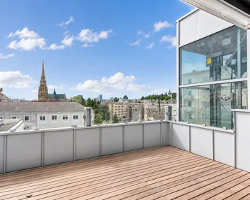 Großer Balkon mit Holzboden und weitem Blick über die Stadt und eine Kirche.