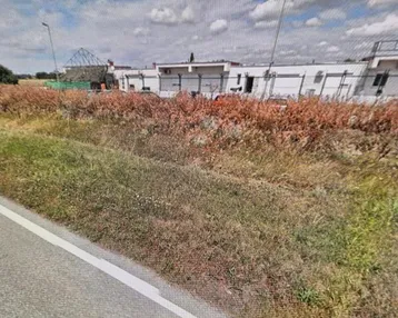 Blick auf ein weißes Gebäude neben einer Straße und einem Feld unter bewölktem Himmel.