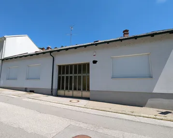 Fassade eines Gebäudes mit Garagentor und Rollläden unter blauem Himmel.