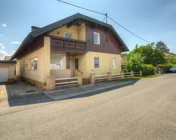 Ansicht des Hauses von der Straße mit Garage und Vorgarten bei sonnigem Wetter.