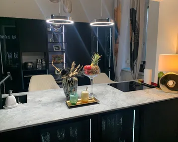 Moderne Küche mit großer Kücheninsel, Induktionskochfeld und eleganten schwarzen Schränken.