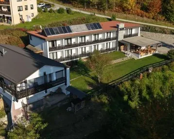 Luftaufnahme von mehreren Gebäuden in einer grünen Landschaft mit Solarpaneelen auf einem Dach.