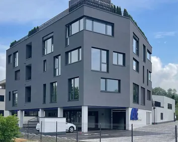 Modernes Bürogebäude mit dunkler Fassade und großen Fenstern, umgeben von einer Baustelle.