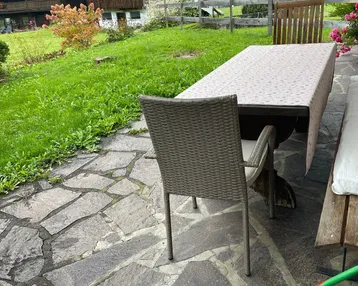 Gepflasterte Terrasse mit Esstisch und Stühlen, umgeben von grüner Landschaft und Häusern.