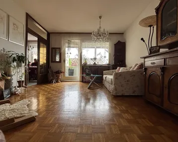 Helles Wohnzimmer mit Parkettboden, Kronleuchter und Zugang zu einem Balkon mit Ausblick.