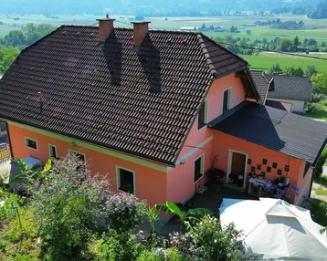 Haus mit Ziegeldach und Gartenbereich, umgeben von grüner Landschaft und Hügeln.