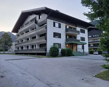 Mehrstöckiges Apartmentgebäude im alpinen Stil mit zahlreichen Balkonen und Bergblick in ländlicher Umgebung.