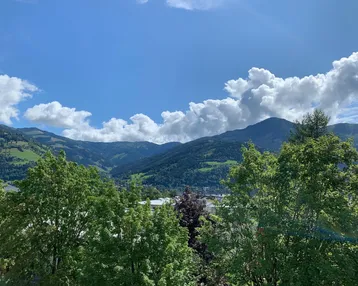 Malerischer Bergblick mit üppiger grüner Vegetation unter blauem Himmel und weißen Wolken.