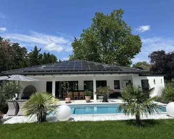 Modernes Einfamilienhaus mit Photovoltaikanlage, großem Pool und gepflegtem Garten unter blauem Himmel.