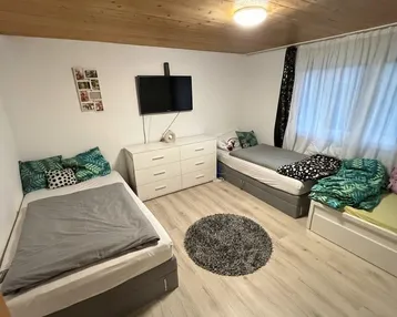 Helles Schlafzimmer mit zwei Einzelbetten, Holzdeckenverkleidung und Laminatboden.