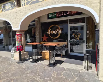 Außenansicht eines Cafés mit Sitzgelegenheiten unter einem Bogen und Blick auf die Straße.
