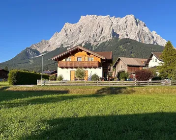 Charmantes Haus im alpinen Stil mit Holzbalkonen und beeindruckendem Bergblick an einem sonnigen Tag.