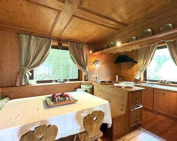 Traditionelle Holzküche mit Essbereich, Holztäfelung und Blick ins Grüne durch die Fenster.