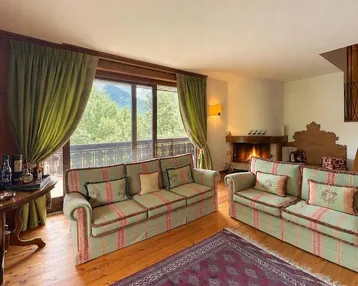 Gemütliches Wohnzimmer mit Kamin, bequemen Sofas und Zugang zum Balkon mit Bergblick.