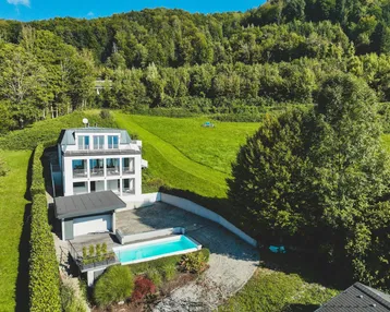 Moderne Villa mit Infinity-Pool und weitläufigem Blick auf die umliegende grüne Landschaft und den See.