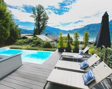 Geräumige Terrasse mit Pool und bequemen Liegestühlen, die einen atemberaubenden Blick auf den See und die Berge bietet.