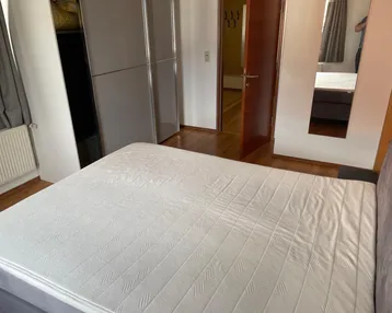 Helles Schlafzimmer mit Holzboden, großem Bett und praktischem Einbauschrank für Stauraum.