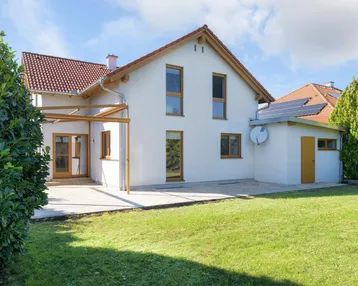 Hinteransicht eines modernen Einfamilienhauses mit großem Garten, Terrasse und einem Anbau mit Solaranlage.