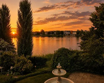 Malerischer Sonnenuntergang über dem See, mit einem charmanten Garten und Springbrunnen im Vordergrund.