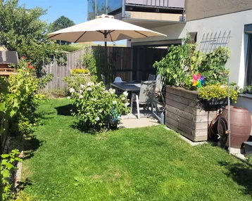 Gepflegter Gartenbereich mit Rasenfläche, Sitzgelegenheiten und Sonnenschirm für entspannte Stunden im Freien.