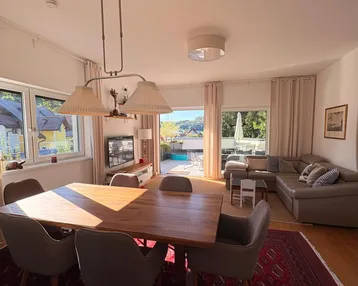 Heller Wohn- und Essbereich mit Holztisch, bequemer Couch und Zugang zur großen Terrasse.