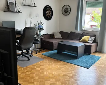 Helles Wohnzimmer mit Parkettboden, Sofa, Schreibtisch und Blick ins Grüne.