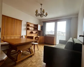 Gemütlicher Wohn-Essbereich mit traditionellen Holzmöbeln, Parkettboden und Zugang zum Balkon.