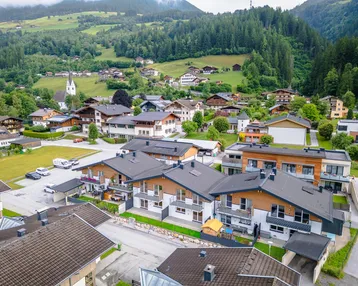 Luftaufnahme einer modernen Wohnsiedlung mit Reihenhäusern vor einer malerischen Bergkulisse.