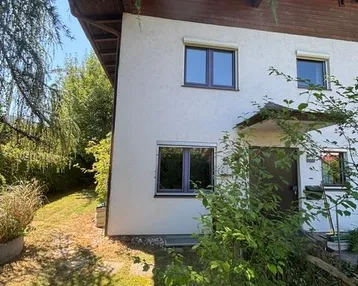 Vorderansicht eines Hauses mit weißer Fassade, braunem Dachüberstand und grüner Umgebung.