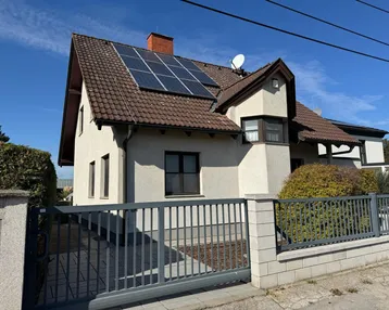 Einfamilienhaus mit Satteldach, Solaranlage und gepflegtem Vorgarten unter blauem Himmel.