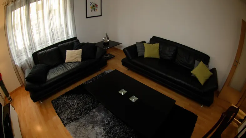 Geräumiges Wohnzimmer mit zwei schwarzen Ledersofas, dunklem Teppich und hellem Parkettboden.