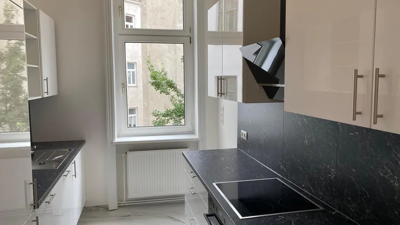 Moderne Küche mit weißen Hochglanzfronten, dunkler Arbeitsplatte und Induktionskochfeld.